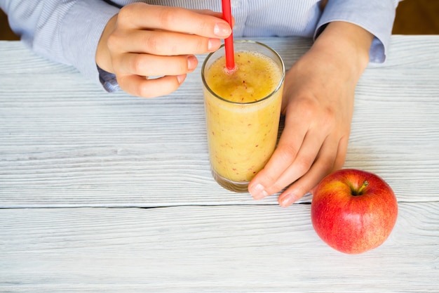 Mujer bebe batidos de manzanas y apio en un vaso con una pajita en una mesa