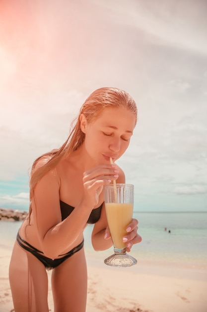 Una mujer bebe un cóctel en la playa.