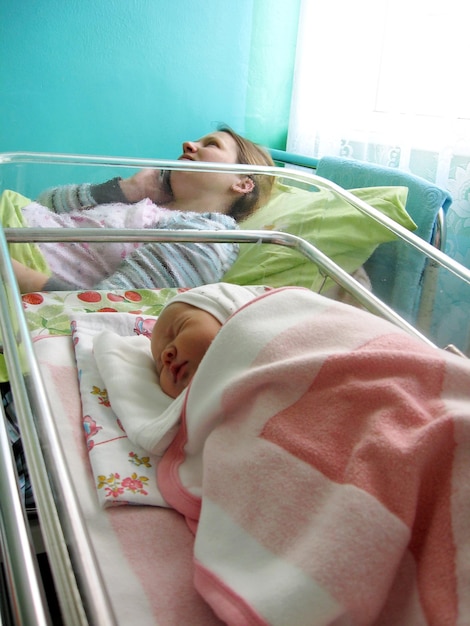 Mujer con bebé recién nacido en el hospital de maternidad Mamá y bebé recién nacido en el hospital de maternidad Bebé recién nacido acostado en una cama pequeña y madre recibiendo felicitaciones