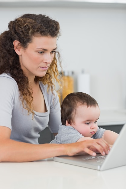 Mujer con bebé usando la computadora portátil en el mostrador