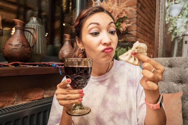 una mujer bebe vino georgiano y come cocina tradicional khinkali en un restaurante