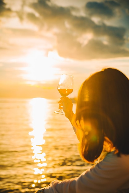 Mujer bebe vino en la playa mirando el atardecer