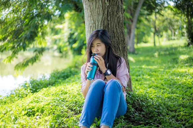 mujer bebiendo agua en el parque, joven pelirroja sedienta bebiendo agua de una botella en verano