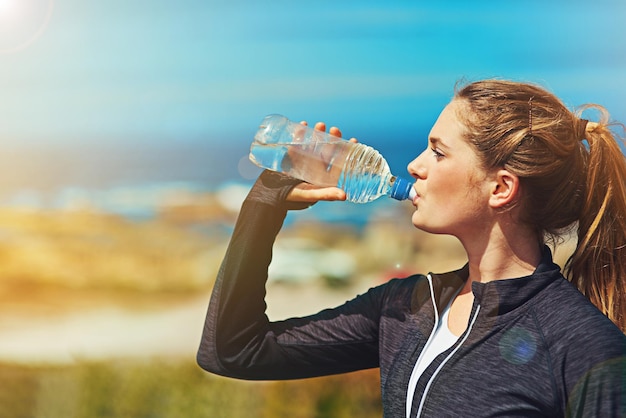 Mujer bebiendo agua, salud y estado físico en la naturaleza, cielo azul y atleta al aire libre con hidratación y espacio para maquetas. Ejercicio en la playa.