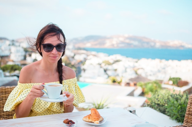 Mujer bebiendo café caliente en la terraza del hotel de lujo con vistas al mar en el restaurante del complejo.