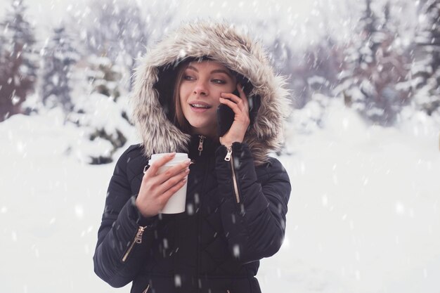 Mujer bebiendo café o té caliente de taza bajo copos de nieve en invierno