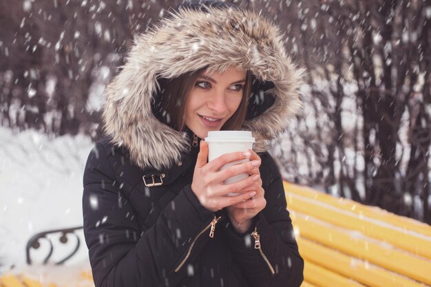 Mujer bebiendo café o té caliente de taza bajo copos de nieve en invierno