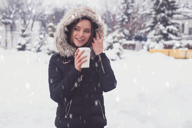 Mujer bebiendo café o té caliente de taza bajo copos de nieve en invierno