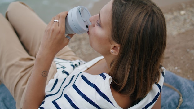 Mujer bebiendo café de picnic en el borde del acantilado primer plano chica pensativa descanso orilla del mar