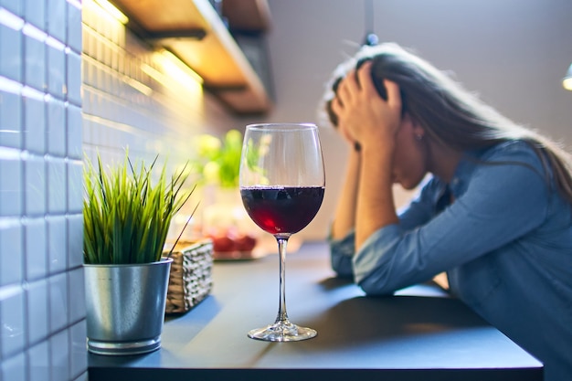 Mujer bebiendo deprimida solitaria que sufre de abuso de adicción al alcohol con copa de vino tinto sola en casa.