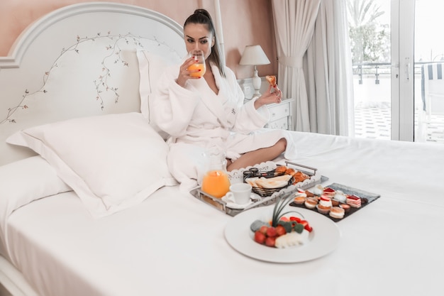Foto mujer bebiendo jugo durante el desayuno en la cama