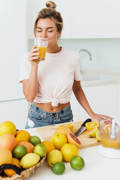 Mujer bebiendo jugo de naranja casero recién exprimido en cocina blanca