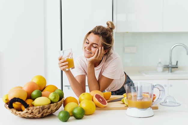 Mujer bebiendo jugo de naranja casero recién exprimido en cocina blanca