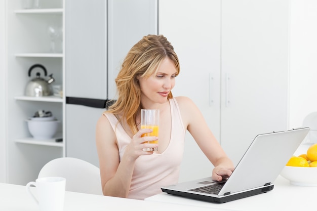 Mujer bebiendo mientras ella está mirando su computadora portátil
