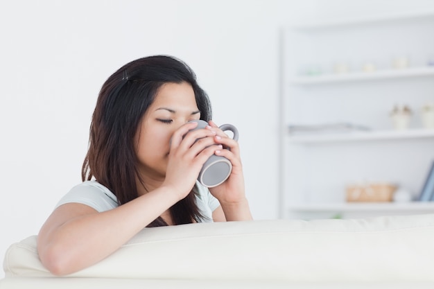 Mujer bebiendo de una taza mientras lo sostiene con las dos manos