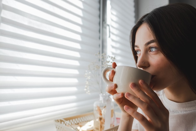 Mujer bebiendo té sentado en la ventana, disfrutar de la vida en una soleada mañana de primavera