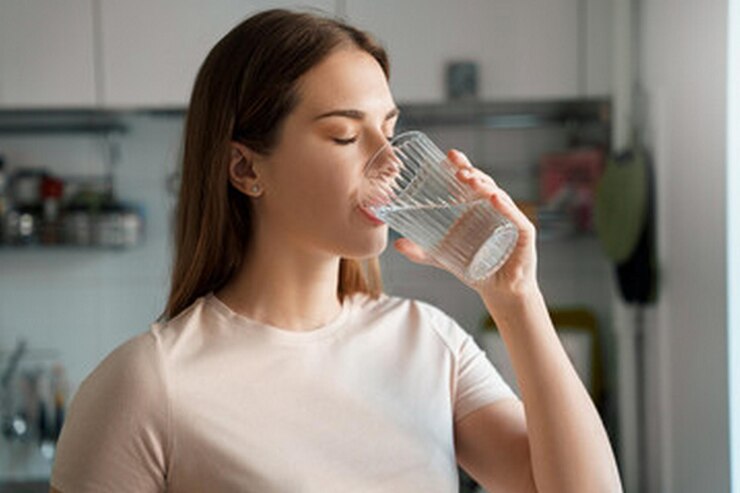 una mujer bebiendo de un vaso de agua con una camisa blanca