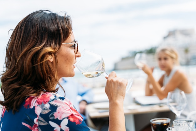 Mujer bebiendo vino con otras personas en la terraza de un restaurante frente al mar