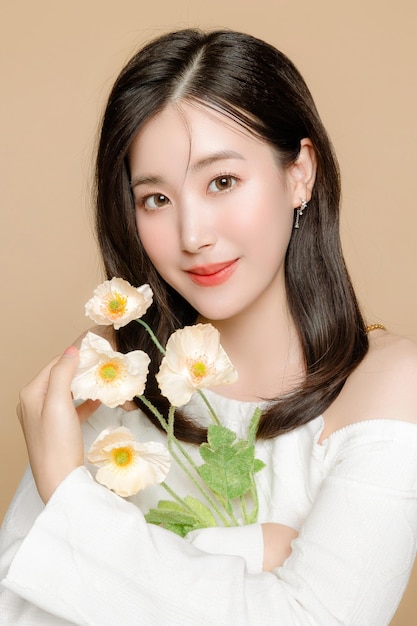 Mujer de belleza asiática joven cabello corto con estilo de maquillaje coreano en la cara y piel fresca clara perfecta con flor sobre fondo beige aislado Tratamiento facial Cirugía plástica de cosmetología