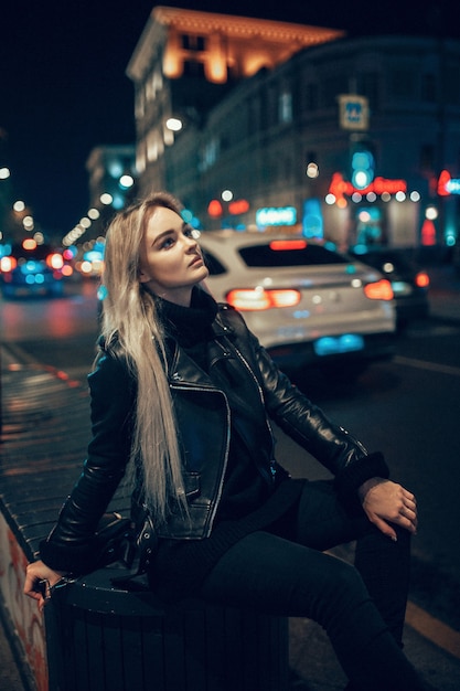 Mujer de belleza joven sexy posando sobre fondo de calle iluminada ciudad de noche. Vacaciones de vacaciones. Rubia joven elegante con pelo largo