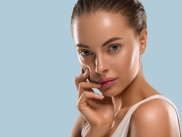 Mujer de belleza con manos naturales sanas componen la piel limpia y fresca concepto color de fondo azul