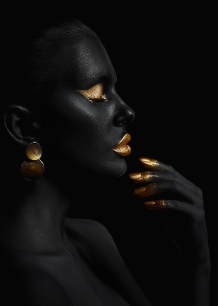 Mujer de belleza pintada en arte corporal de color de piel negra, párpados de labios de maquillaje dorado, uñas de puntas de dedos en pintura de color dorado. maquillaje profesional dorado