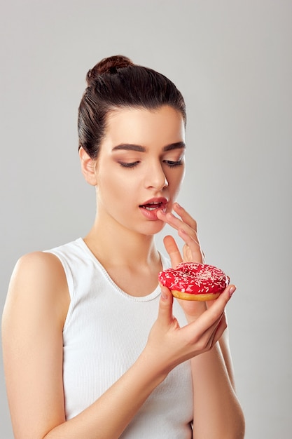 La mujer de la belleza sostiene un postre rosado. Dieta. Gracioso. Chica modelo morena gustos y comiendo un postre