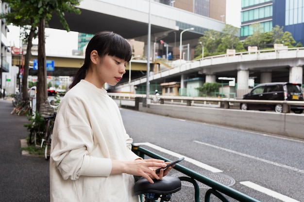 Mujer con bicicleta eléctrica en la ciudad con smartphone