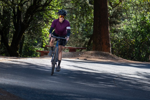 Mujer en bicicleta de pista en una carretera en medio del concepto de deporte al aire libre del bosque