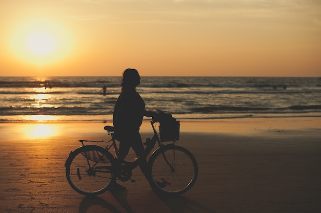 Mujer con bicicleta en la playa al atardecer