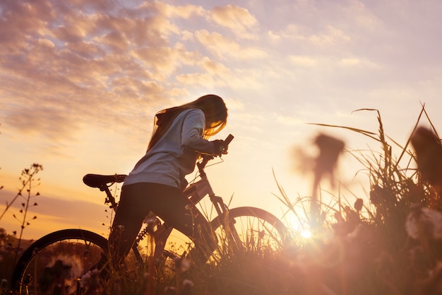 Mujer con bicicleta en puesta de sol