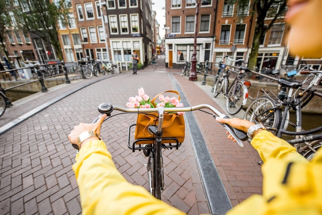 Mujer en bicicleta con ramo de flores en la calle en la ciudad de Amsterdam. Ver en las manos sosteniendo el timón