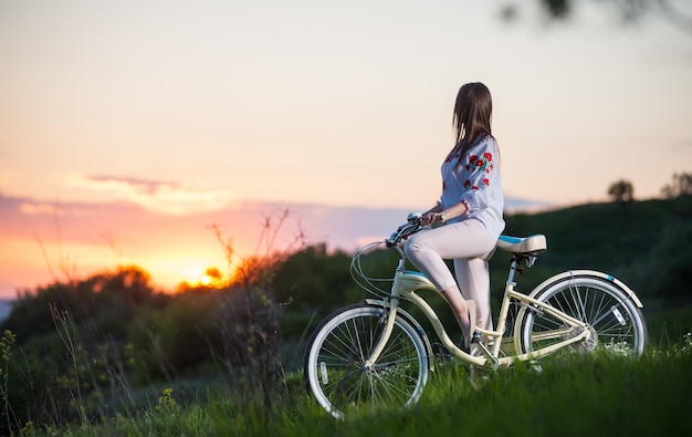 Mujer con bicicleta retro en la colina en la noche