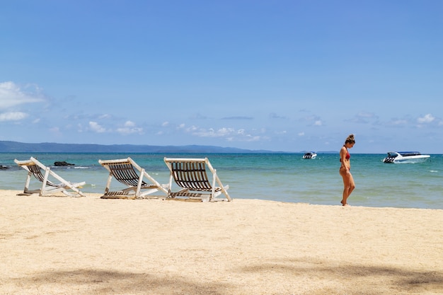 Mujer con bikini y caminando por la playa del lado derecho.