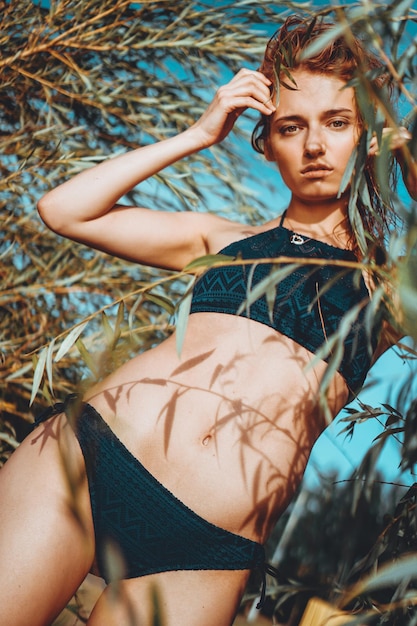 Mujer en bikini en una playa tropical con plantas - horario de verano