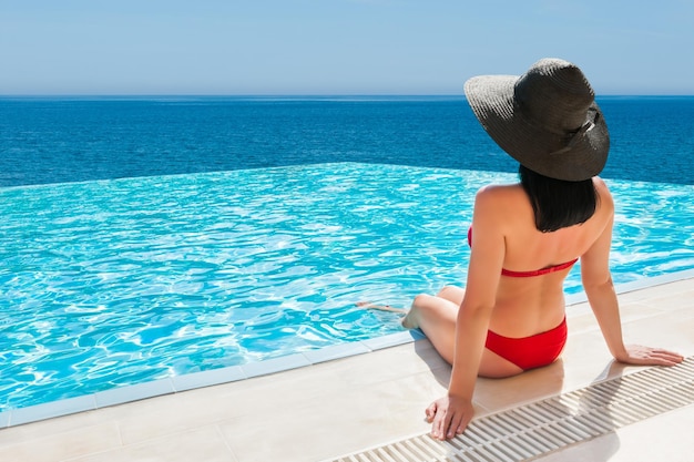 Mujer en bikini rojo relajándose en la piscina infinita con vista al mar Viajes y vacaciones