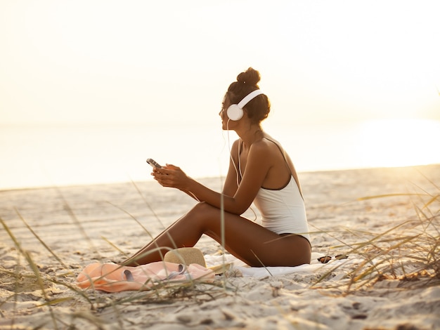 Mujer en Bikini con un smartphone y auriculares en la playa