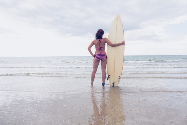 Mujer en bikini con tabla de surf en la playa