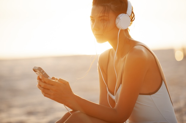 Mujer en Bikini con un teléfono inteligente y auriculares en la playa