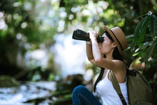 Mujer con binoculares y telescopio en selva tropical. Senderismo en verano.