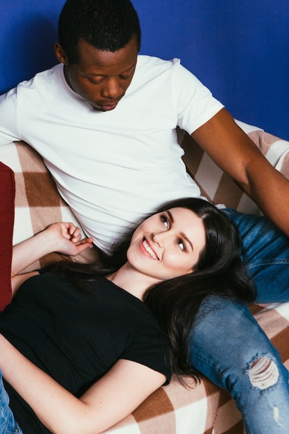 Mujer blanca y hombre negro feliz de descansar en el sofá en casa, joven pareja internacional de ocio, hablando, concepto de felicidad