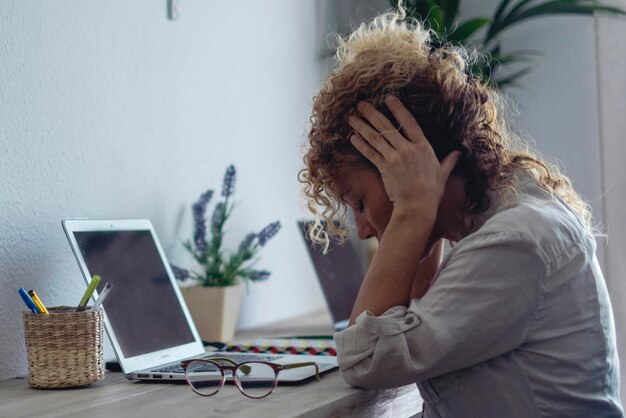 Foto mujer blanca joven enferma trabaja en la computadora en la oficina de casa se quita las gafas sufre de migraña o dolor de cabeza mujer millennial infeliz y cansada lucha con mareos o visión borrosa usando portátil