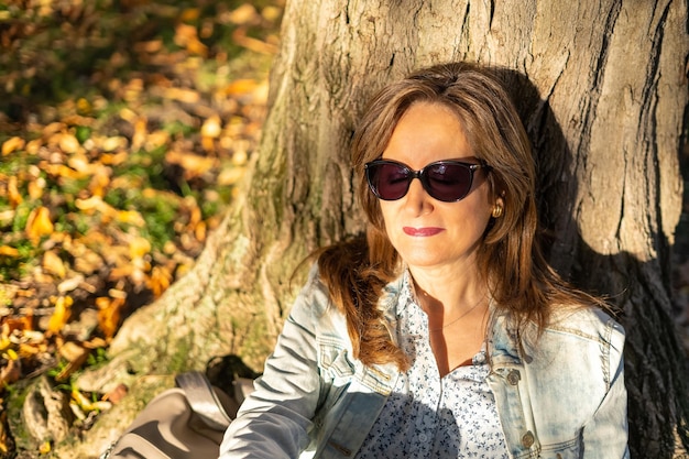 Mujer blanca madura disfrutando del sol sentada en el césped del parque con el reflejo del sol en la cara