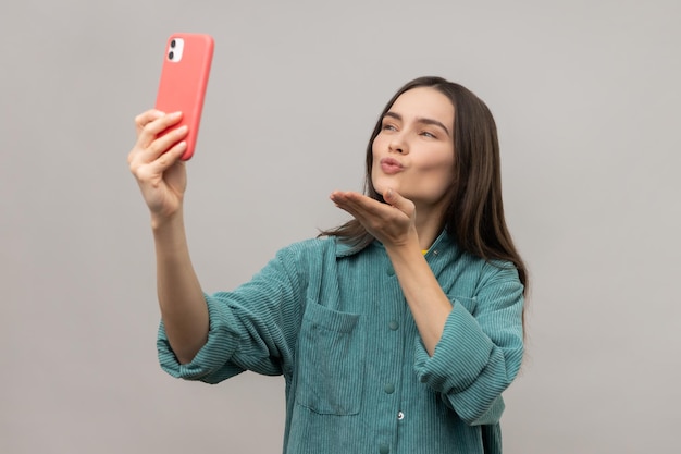 Mujer bloguera enviando un beso de aire a un teléfono inteligente comunicándose por videollamada tomando selfie