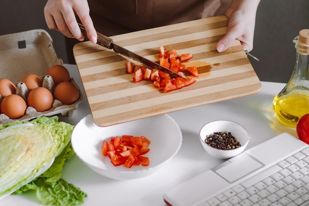 Mujer bloguera preparando ensalada de verduras dietéticas en casa Lecciones de cocina en línea usando una computadora portátil en la cocina
