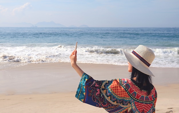 Mujer en blusa colorida que toma fotos de Selfie en la playa de Copacabana, Río de Janeiro