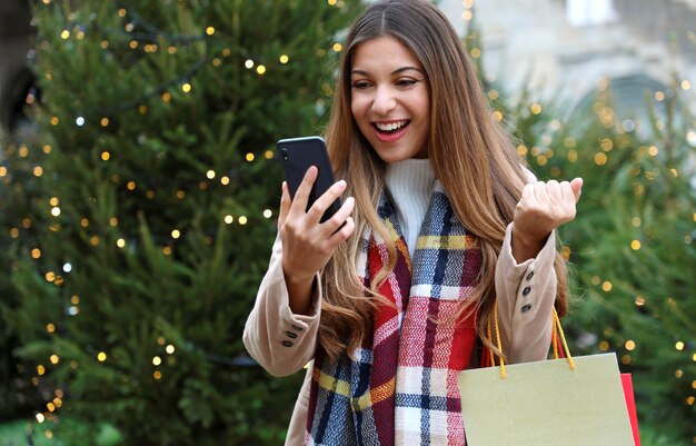 Mujer con bolsas de la compra en la mano comprando regalos de Navidad con su teléfono inteligente.