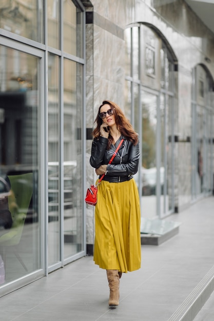 Mujer con bolso rojo caminando mientras habla por teléfono cerca de un edificio comercial