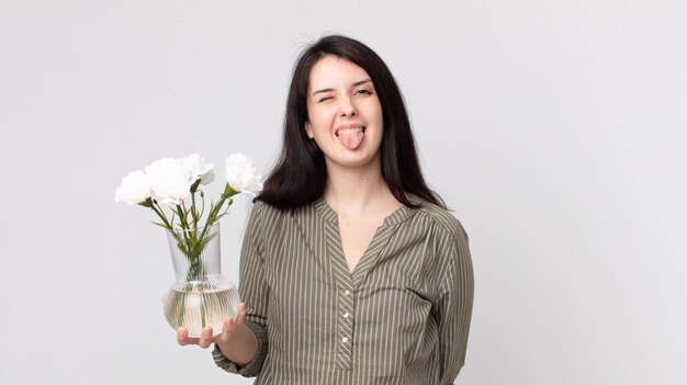 Mujer bonita con actitud alegre y rebelde, bromeando y sacando la lengua y sosteniendo flores decorativas. agente asistente con un auricular