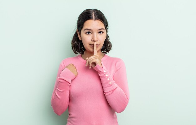 Mujer bonita adolescente que parece seria y cruzada con el dedo presionado en los labios exigiendo silencio o silencio guardando un secreto